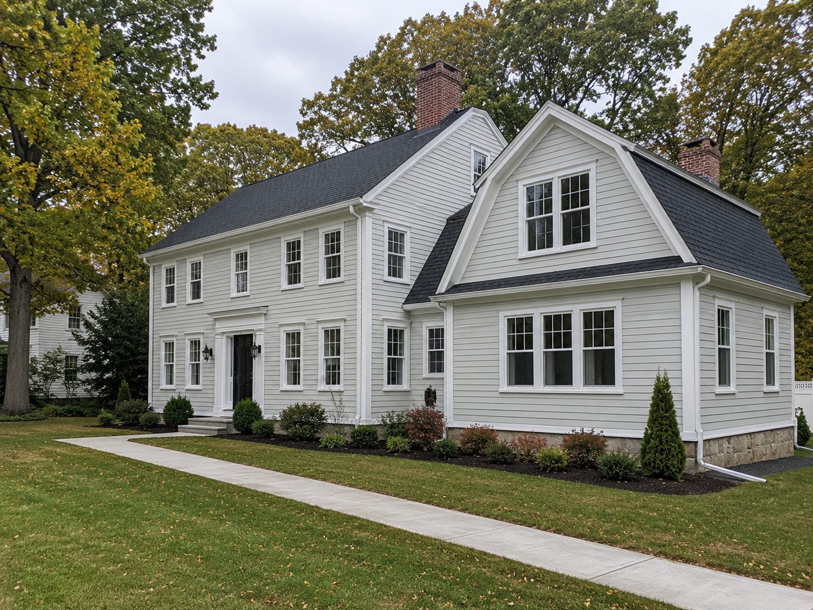 Freshly completed colonial home exterior with new framing and an addition visible alongside mature deciduous trees